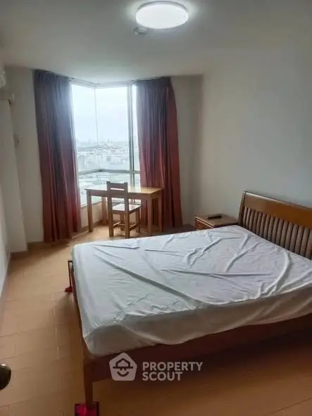 Cozy bedroom with city view and natural light, featuring a wooden bed and small desk.