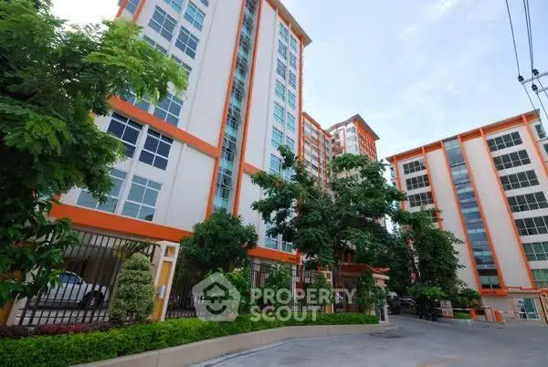 Modern apartment building with lush greenery and spacious parking area.
