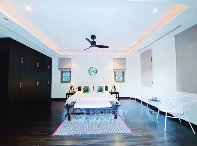 Spacious modern bedroom with dark wood flooring and stylish ceiling fan.