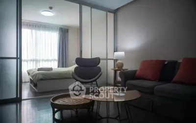 Modern living room with stylish furniture and a view into a cozy bedroom through sliding glass doors.