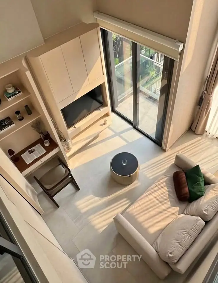 Modern living room with high ceiling and large windows offering natural light and a cozy seating area.