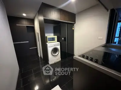 Modern kitchen with sleek black tiles and built-in appliances, featuring a washing machine and stovetop.