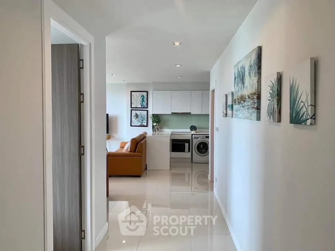 Modern apartment hallway leading to a stylish living room with integrated kitchen and laundry area.