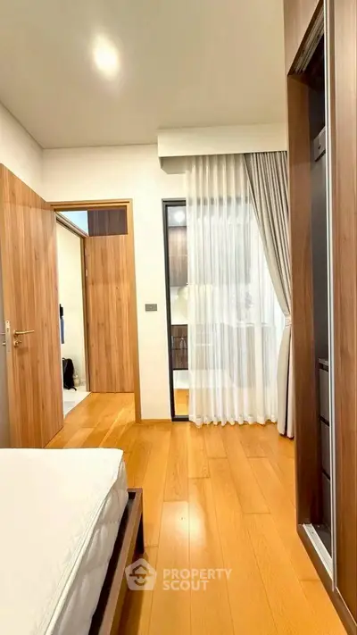 Modern bedroom with wooden flooring and large window with sheer curtains