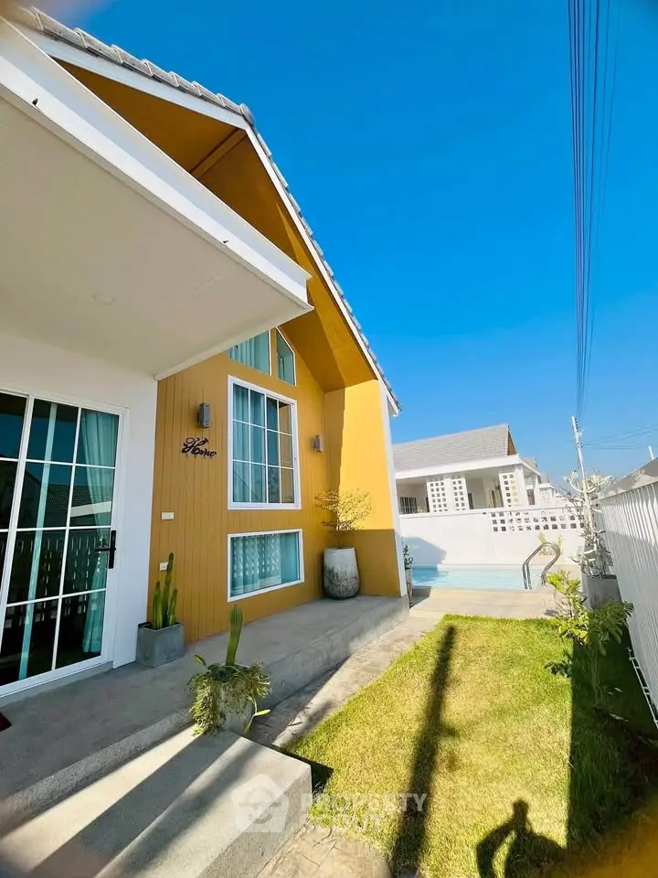Charming yellow house with modern design and spacious outdoor area under clear blue sky.