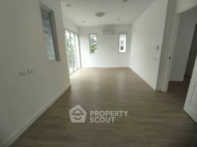 Spacious empty room with wooden flooring and large windows for natural light.