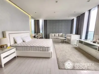 Luxurious spacious bedroom with modern white furniture, plush king-sized bed, and elegant sitting area bathed in natural light from floor-to-ceiling windows.