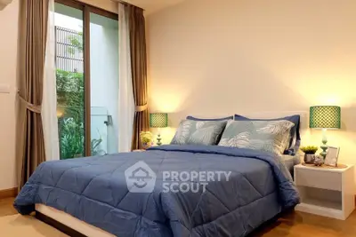 Cozy bedroom with blue bedding, elegant lamps, and garden view through glass doors.