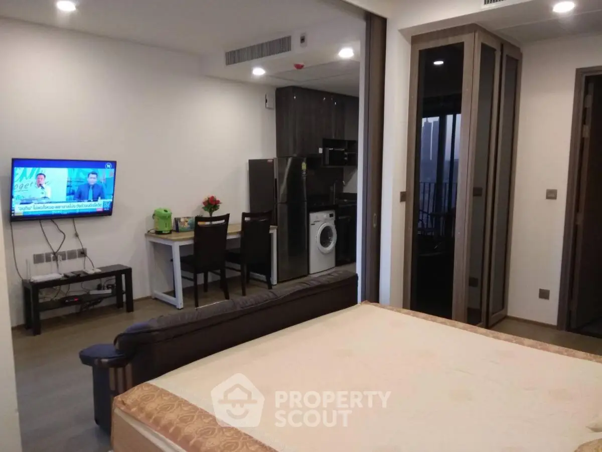 Modern studio apartment with integrated kitchen and living area, featuring a washing machine and flat-screen TV.