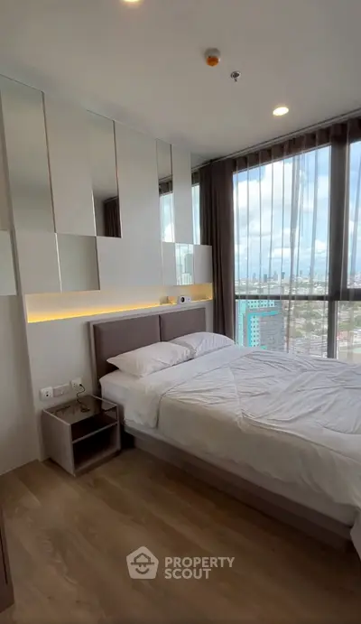 Modern bedroom with large windows and city view, featuring sleek design and natural light.