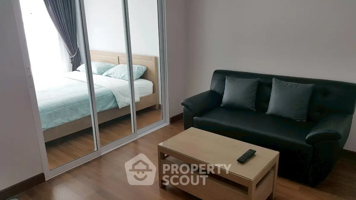 Modern living room with sleek black sofa and mirrored wardrobe reflecting cozy bedroom.