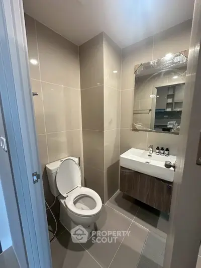 Modern bathroom with sleek fixtures and neutral tiles, featuring a toilet and vanity mirror.