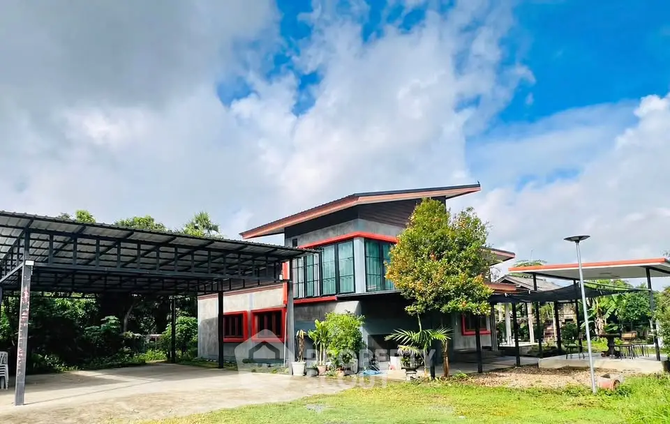 Modern two-story house with large windows and spacious carport in lush green surroundings.