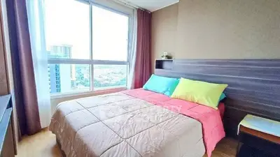 Bright bedroom with large window and colorful bedding in modern apartment.