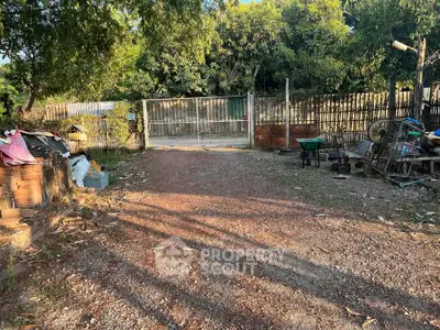 Spacious outdoor area with gravel path and gated entrance, surrounded by lush greenery.