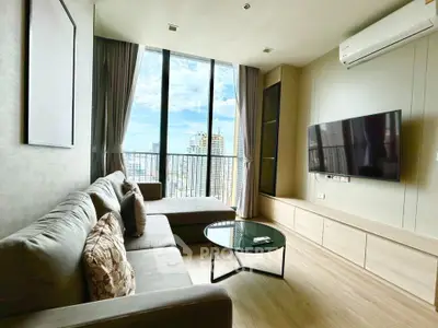 Modern living room with large windows and city view, featuring a comfortable sofa and wall-mounted TV.
