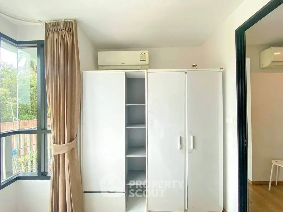 Bright bedroom with large window and white wardrobe, featuring air conditioning for comfort.