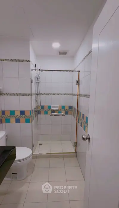 Modern bathroom with colorful tile accents and glass shower enclosure.