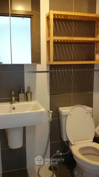 Modern bathroom with sleek sink and toilet, featuring stylish tile design and wooden shelf.