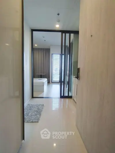Modern apartment hallway leading to a bright bedroom with large windows and sleek design.