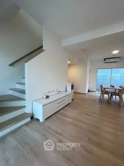 Spacious modern living area with dining set and staircase, featuring sleek wooden flooring and bright natural light.
