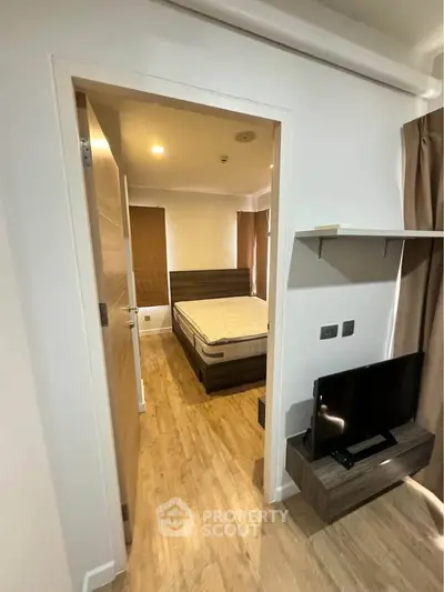 Modern bedroom with wooden flooring and sleek furniture, featuring a cozy bed and a flat-screen TV.