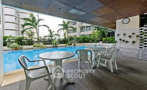 Luxurious poolside area with seating in a modern residential complex, surrounded by lush greenery.