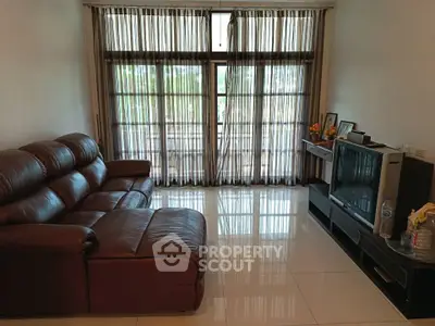 Spacious living room with leather sofa and large windows offering natural light.