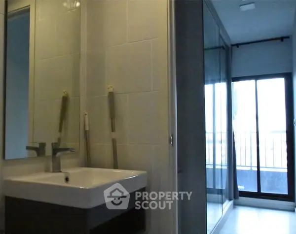 Modern bathroom with sleek sink and large mirror, adjacent to a balcony with glass doors.