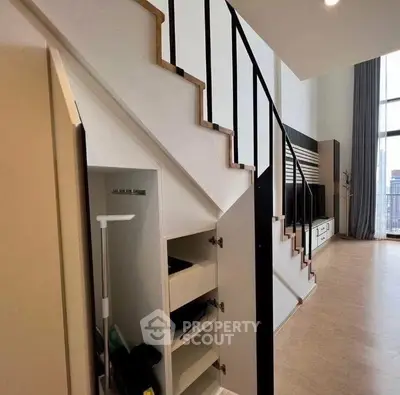 Modern duplex interior with stylish staircase and built-in storage, featuring high ceilings and large windows.