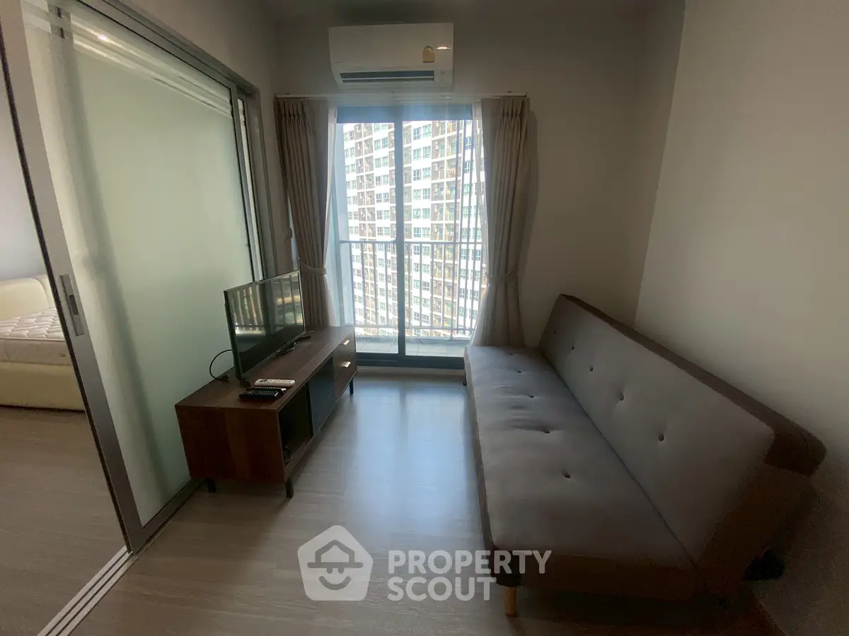 Modern living room with sleek sofa and TV, featuring floor-to-ceiling windows and sliding glass doors.
