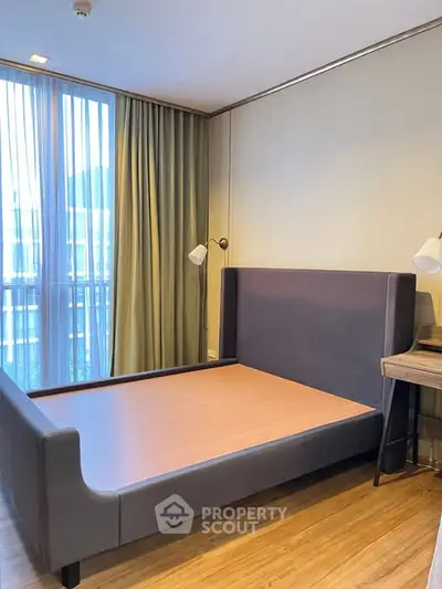 Spacious bedroom with modern bed frame and natural light from large window.