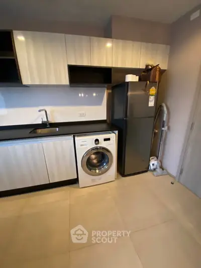 Modern kitchen with sleek cabinets, washing machine, and fridge in a compact layout.