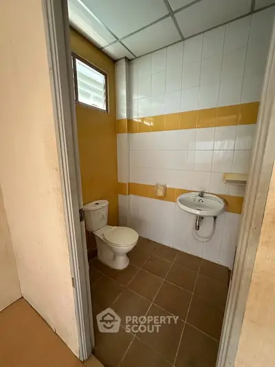 Compact bathroom with yellow and white tiles, featuring a toilet and sink.