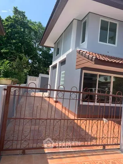 Charming two-story house with tiled roof and gated driveway, surrounded by lush greenery.