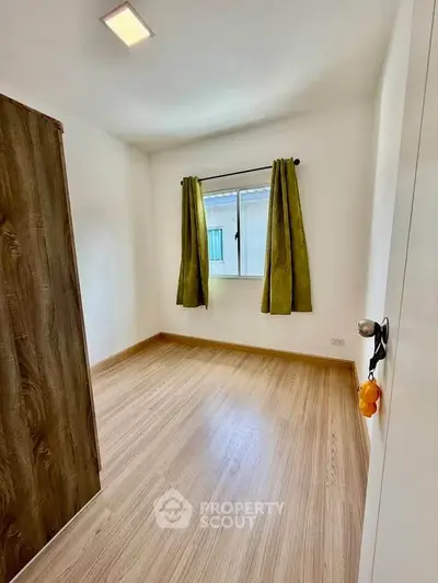 Bright empty room with wooden flooring and green curtains, perfect for customization.