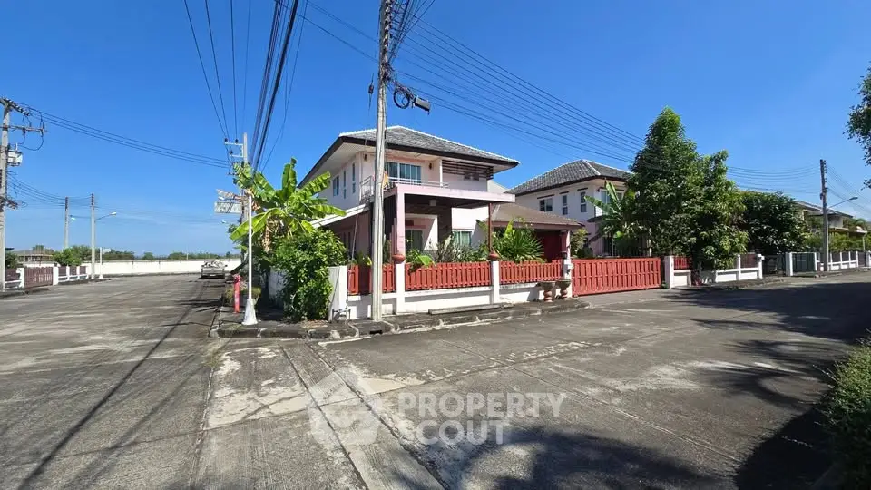 Charming suburban house with red fence and lush greenery on a sunny day.