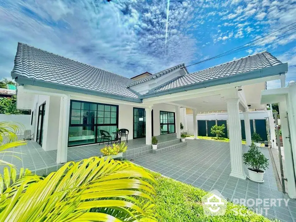 Stunning modern home with spacious tiled patio and lush greenery under a vibrant sky.