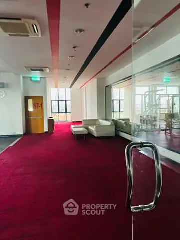 Spacious modern gym with red carpet and white sofas, ideal for fitness enthusiasts.
