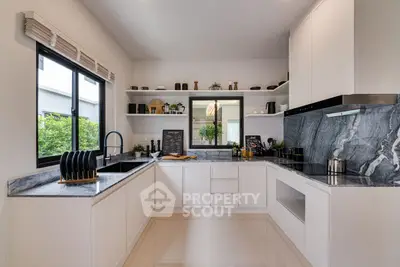 Modern kitchen with sleek white cabinets and marble countertops, featuring an open layout and large window.