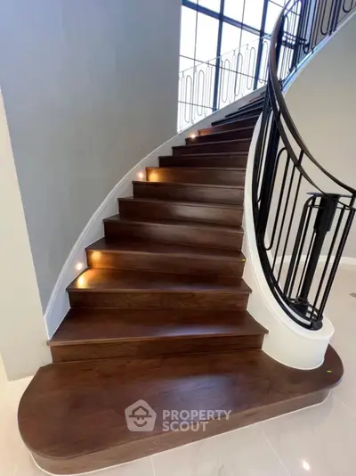 Elegant curved staircase with modern railing and built-in step lighting in luxury home.