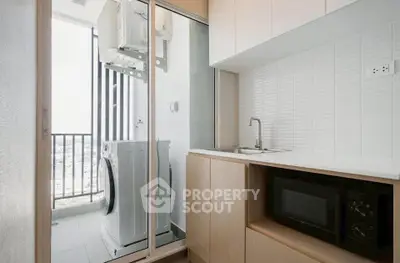Modern kitchen with washing machine and microwave, featuring sleek cabinetry and balcony view.