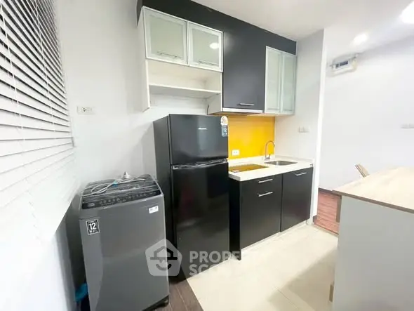 Modern kitchen with black cabinets, fridge, and washing machine in compact layout.