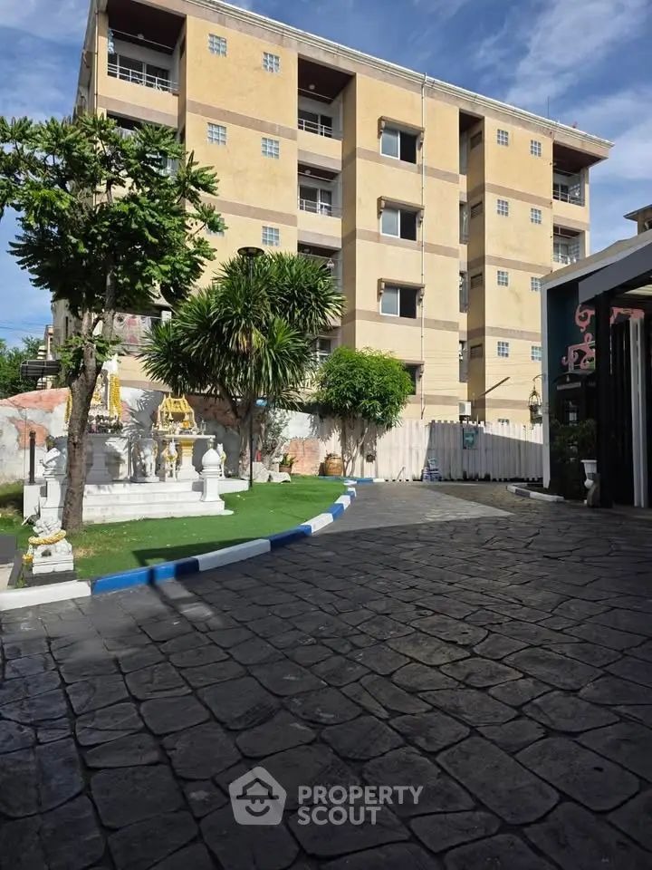 Charming residential building with lush greenery and paved driveway under a clear blue sky.