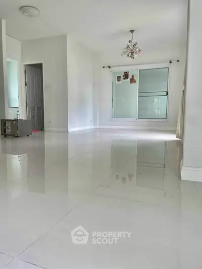 Spacious empty living room with glossy tiled floors and modern chandelier.