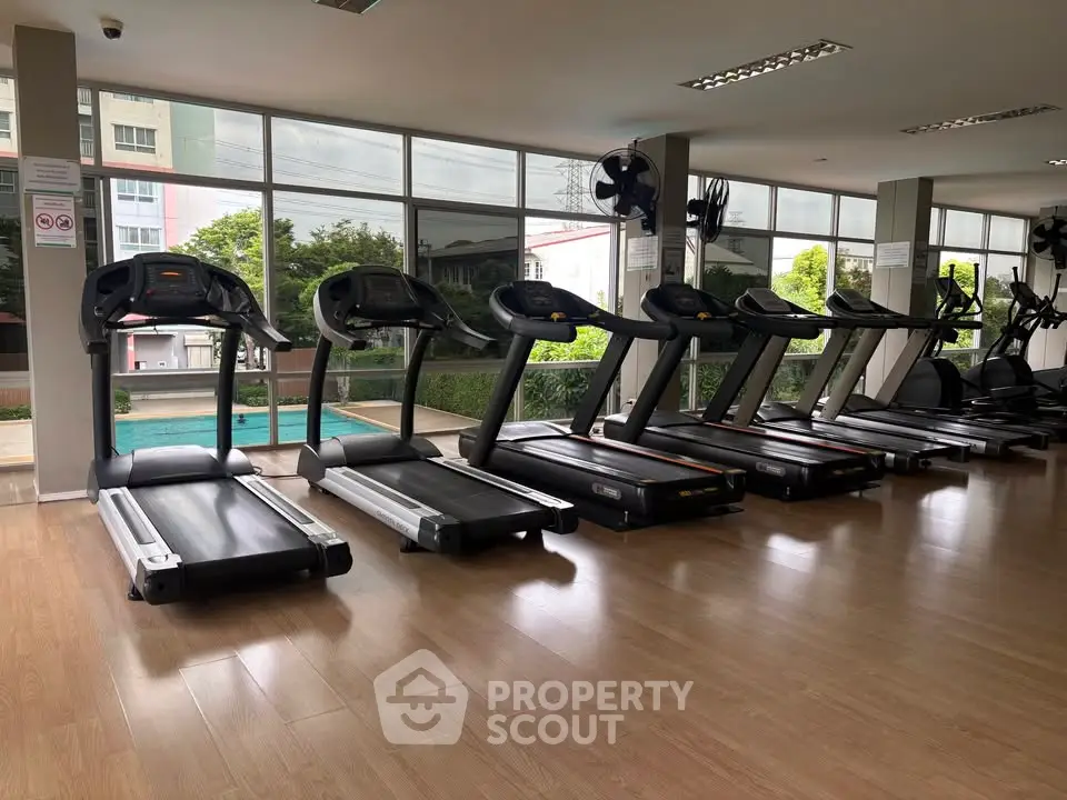 Modern gym with treadmills and pool view in luxury apartment complex.