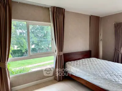 Bright bedroom with large window and garden view, featuring a wooden bed and elegant curtains.