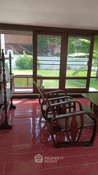 Charming living room with vintage wooden furniture and large windows overlooking a lush garden.