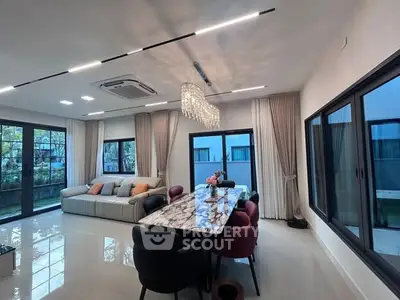 Luxurious living room with elegant marble dining table and modern lighting, featuring large windows and garden view.