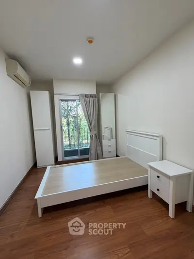 Spacious bedroom with balcony view, featuring modern white furniture and wooden flooring.